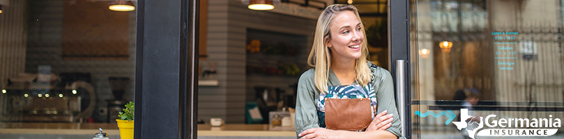 A woman standing in front of her small business with her arms crossed.