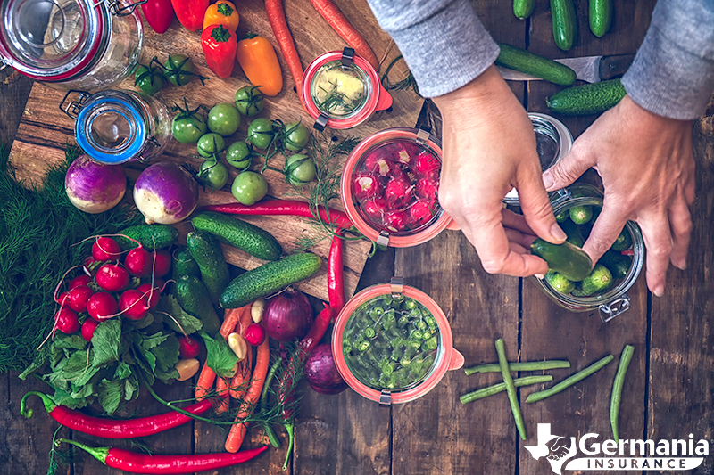 Hands placing vegetables in jars to preserve a garden harvest.