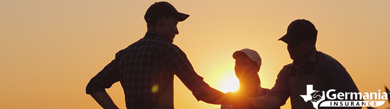 A Texas farmer shaking hands in a field with a farm and ranch insurance agent.