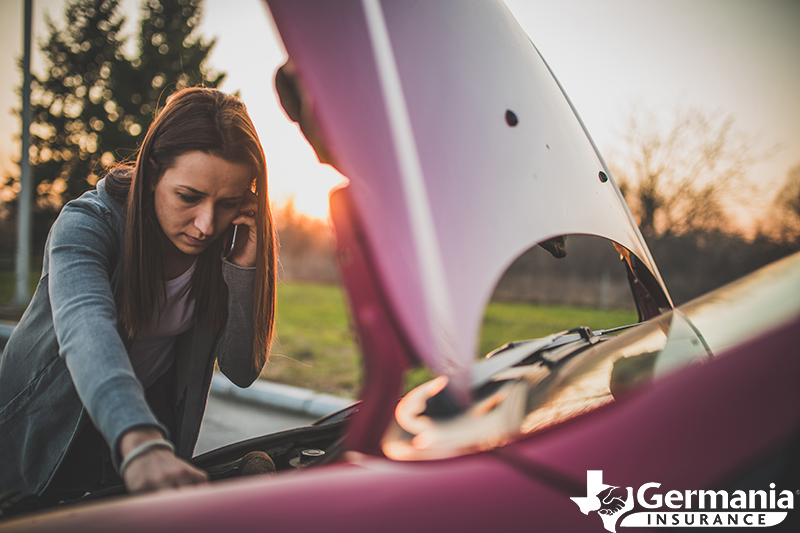 A women inspecting her car's engine after a breakdown on the side of the road.